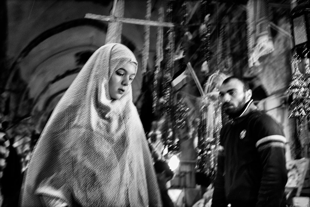 A woman wearing a light headscarf passing a young man.